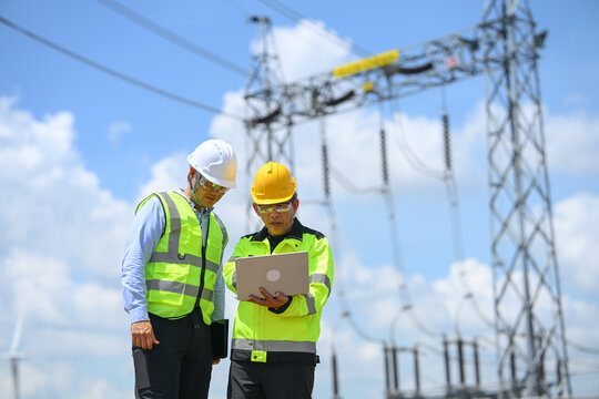 Electrical engineer and technician inspecting substation equipment during outdoor power grid maintenance, wearing safety helmet and reflective vest under bright blue sky