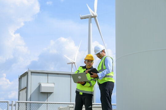 Wind turbine engineer electrical technician inspecting renewable energy equipment at industrial power facility under bright blue sky