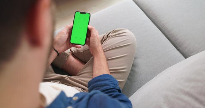 Over the shoulder view of a green screen smartphone on a sofa