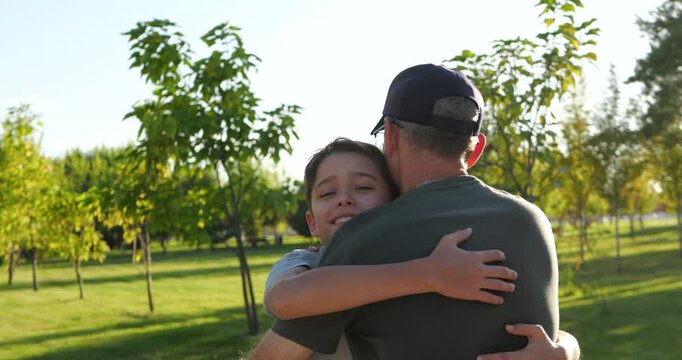 Father and son reunite in sunny park as smiling child embraces dad. Loving family hug shows joy, trust, and connection. Warm summer sunlight creates emotional outdoor memory for family storytelling.