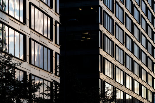 Opposing modern office facades framing a deep shadowed gap in the Wola business district of Warsaw Poland with warm light reflected in rectangular windows