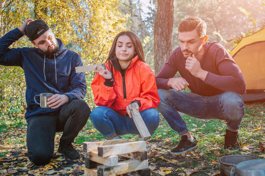 Three friends sitting in squad position and look at brickets of wood. Young woman hold one piece of it. They don't know what to do with it. People are frustrated.
