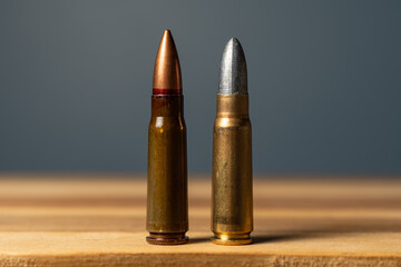 Two 7.62x39mm rifle cartridges side by side on wooden surface comparing standard military full metal jacket ammunition with custom subsonic lead bullet reloading round. © Dmitri