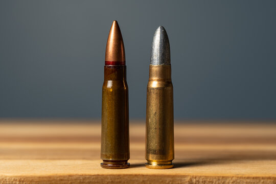 Two 7.62x39mm rifle cartridges side by side on wooden surface comparing standard military full metal jacket ammunition with custom subsonic lead bullet reloading round.