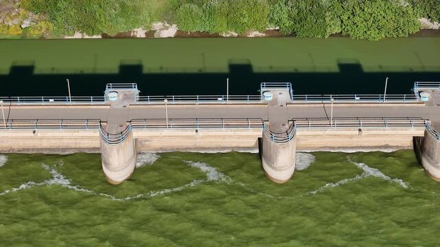 Aerial roll view of a dam wall with turbulent water and shadow of the embankment