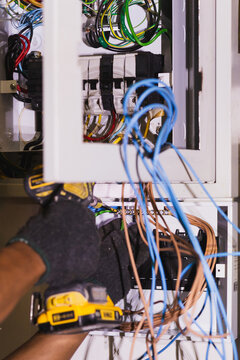 Electrician using an electric screwdriver to secure wires inside an electrical circuit.