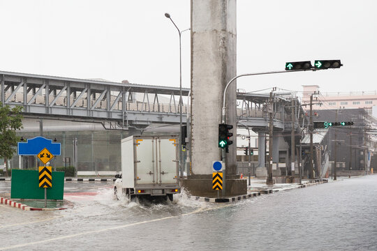 White delivery truck driving through a flooded city street during heavy rain.