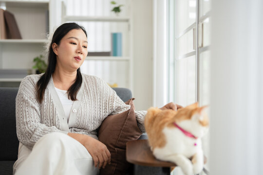 Smiling woman with  Orange tabby cat sitting peacefully by the window in cozy home.