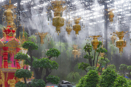 Ornate golden lanterns hanging under roof in tropical greenhouse garden with automated mist cooling system irrigation over bonsai trees. Pattaya, Thailand.