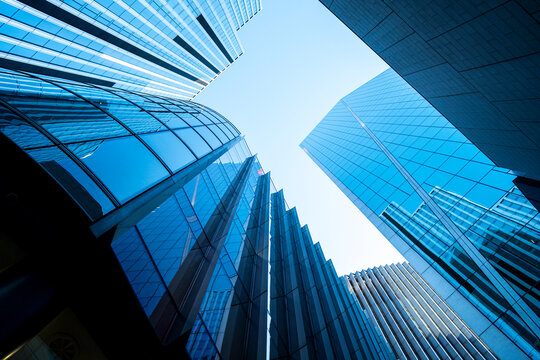Looking upward between blue glass office towers in London where curved and angular facades converge around an open patch of sky in a dramatic perspective