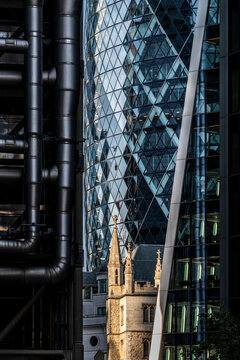 Historic stone church framed by glass skyscrapers and exposed metal pipes in London showing a striking contrast between old architecture and modern offices