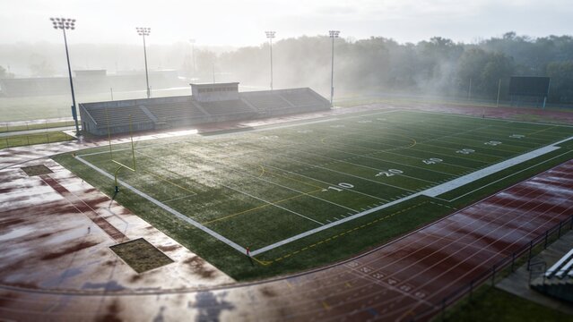 Glowing artificial turf field showing yard lines and wet red track at stadium, with goalposts
