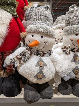 Decoraci&oacute;n navide&ntilde;a. Simp&aacute;tico mu&ntilde;eco de nieve de peluche de color blanco, con foulard, sombrero, botones y nariz de zanahoria color naranja, en estante de tienda
