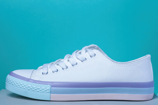 White canvas sneakers with pastel striped blue, purple, pink sole on blue background