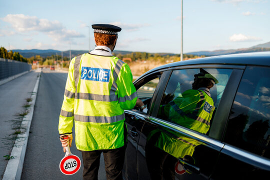 Police officer checks a vehicle at a roadside checkpoint during daylight