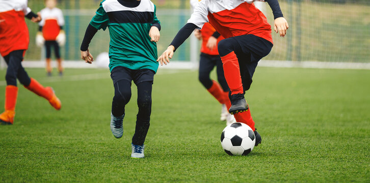 Junior Soccer Players in Green and Red Kits Battling for Ball Possession During Competitive Youth League Match on Grass Pitch