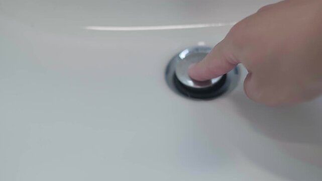 Hand closing pop up sink drain plug to fill basin with water. Close up of modern bathroom plumbing and hygiene routine. Perfect for home improvement, interior design and water conservation.