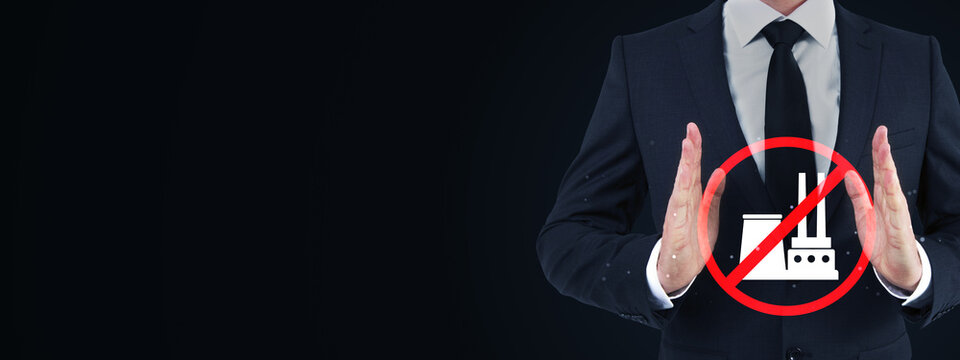 Businessman showing stop gesture beside prohibited factory symbol on dark background with generous copy space for industrial safety concept design.