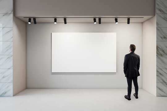 Businessman Viewing a Blank Gallery Exhibition Poster Mockup on Illuminated Interior Wall for Clean Branding Presentation and Marketing Design.