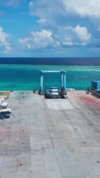 Vertical drone shot of maritime boat hoist lifting a vessel in shipyard slipway next to turquoise ocean. Great for social media, stories, and vertical video promo.