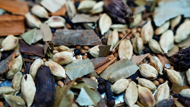 Assorted whole spices with cardamom, cinnamon, and bay leaves, Close-up view of assorted whole spices, including cardamom pods, cinnamon bark, bay leaves, and dark aromatic pods in earthy tones.