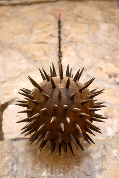 Doha, Qatar - October 10, 2026: Antique iron spiked flail ball hanging from a chain against a rustic stone wall background