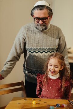 Jewish grandfather and child celebrating hanukkah, playing dreidel game