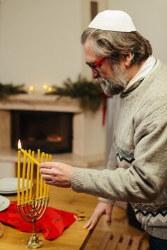 Jewish man lighting hanukkah menorah candles at home