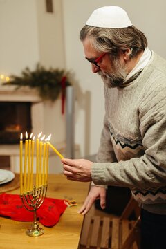 Senior man lighting candles on menorah for hanukkah