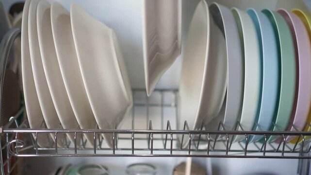 Hand placing a white plate into a kitchen dish rack. Close-up of household organization, dishware storage, kitchen routine, and everyday home activity.
