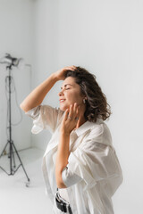 Serene mature woman holding hand on hair with closed eyes in bright photo studio. © Olga