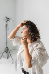 Serene mature woman holding hand on hair with closed eyes in bright photo studio. © Olga