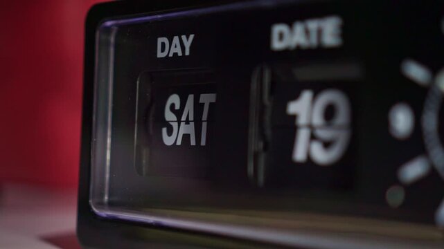 a retro flip clock changing the day and date, with mechanical flaps turning in shallow focus. Ideal for time, calendar, and schedule projects.