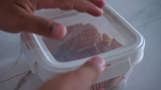 Close-up shot of hand opening snack box filled with biscuits with an airtight lid. Suitable for food storage and kitchen lifestyle themes.