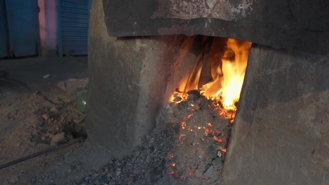 Close-up of a blacksmith forge with flames and glowing coals as a metal piece is heated inside the fire, capturing the heat, tools, and rugged environment of a metalworking workshop.
