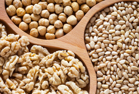 Top view of appetizing shelled nuts on wooden plate: blanched walnuts, hazelnuts, and pine nuts. Organic, healthy, vegetarian food. Edible background. Close-up, flat lay, mockup
