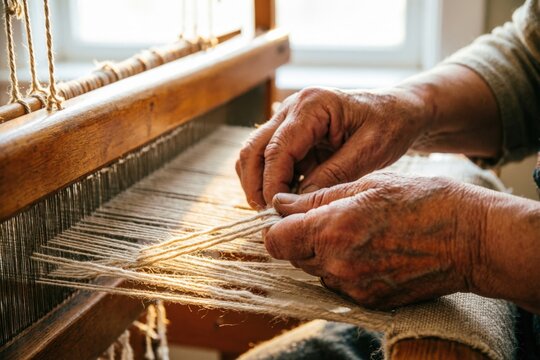 Las manos de un tejedor guiando hilos de lino y lana crudos y sin te&ntilde;ir a trav&eacute;s de un telar de madera