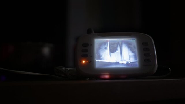 A baby monitor displays infrared video in a dark room close-up. The glowing screen serves as an authentic visual asset for parenting, security, and child care themes.