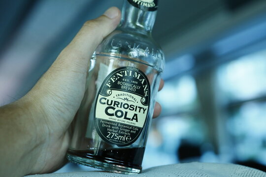 A close-up of a person holding a bottle of botanical brewed cola.