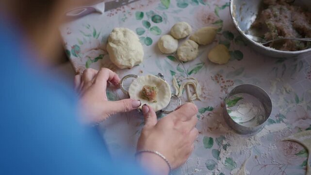 Woman prepares homemade meat dumplings using a metal mold in a home kitchen overhead. The overhead angle captures the authentic culinary workflow of adding meat filling into dough.