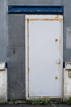 Rusty white metal door surrounded by perforated metal panels and blue painted trim