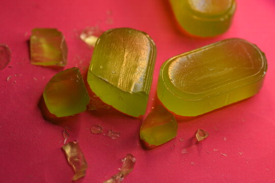 Macro shot of broken and crushed green translucent hard candies with sharp shards and crumbs on a vibrant pink surface. Creative confectionery mess.