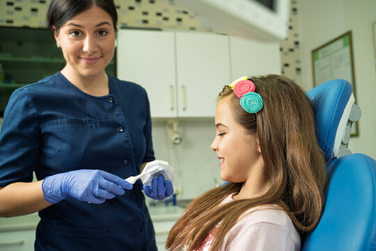 Friendly female dentist reminds you to wash your teeth everyday, looking at you while holding teeth model  