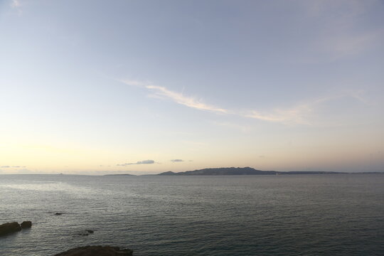 A panoramic view of the calm ocean and distant island at dusk in Okinawa.