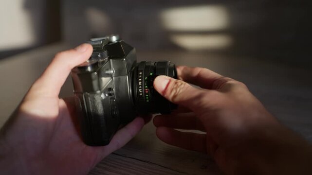 Hands mount and adjust vintage optics on a retro SLR body in warm sunlight. Smooth manual twisting of the focus ring offers authentic mechanical tactile detail for filmmaking tutorials.