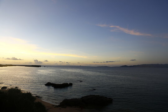 A scenic sunset view of the calm ocean and rocky coastline in Okinawa.