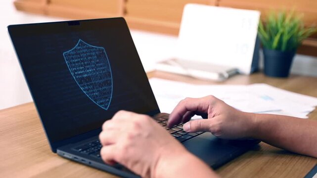 Close up of person hands typing on laptop computer with cyber security shield icon on screen. Data protection, network security, software development and internet technology workplace concept
