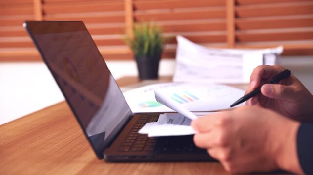 Business man analyzing financial charts and marketing data reports while working on a laptop at the wooden office desk. Professional corporate workplace environment and data analysis concept