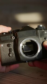 Hands carefully inspect an analog SLR body during equipment maintenance in a studio close-up. The detailed check of the reflex mirror mechanism serves gear repair and restoration tutorials.