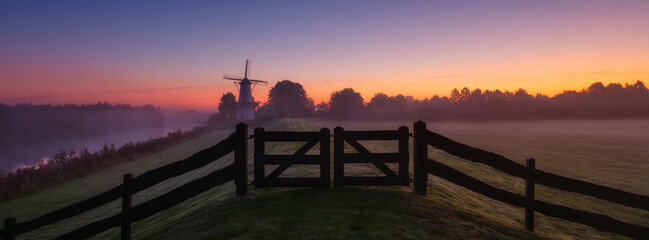 Naklejka premium Panoramic scene. Windmills in the Netherlands during foggy sunrise. Field and meadow. Fence on the field. Natural landscape.